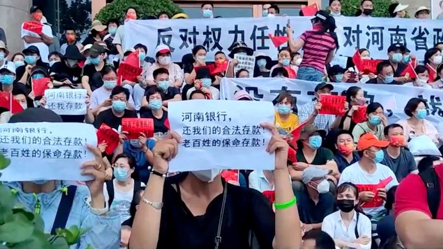 Demonstrators hold up signs during a protest over the freezing of deposits by some rural-based banks, outside a People's Bank of China building in Zhengzhou, Henan province, China, 10 July 2022, in this screengrab from video obtained by Reuters. Text in foreground reads, "Henan Bank, return to us our legal deposits! The people's life-saving deposits!" (Reuters TV via Reuters)
