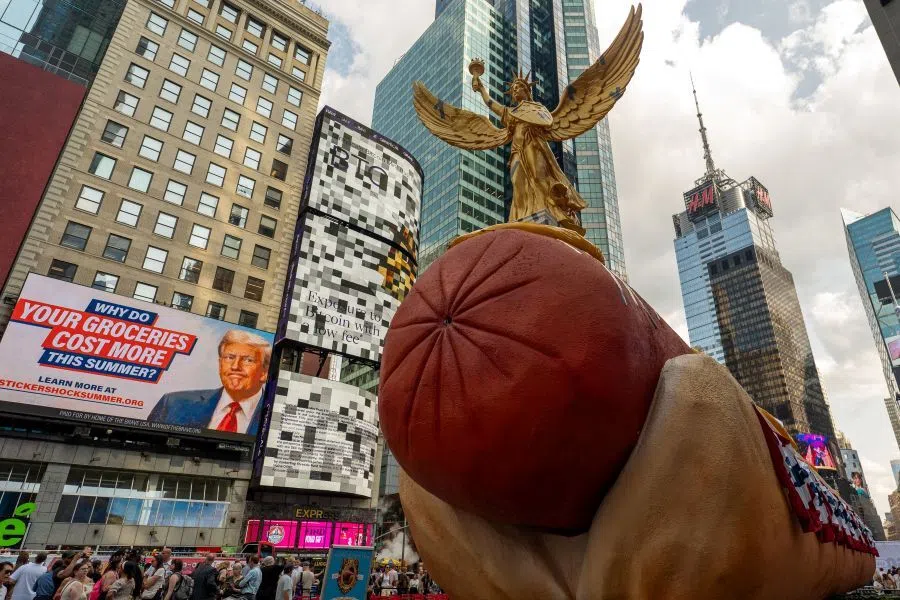 A billboard depicting US President Donald Trump is seen behind a statue of a winged Lady Liberty by Artists Jen Catron and Paul Outlaw prior to the unveiling of an updated version of their viral 65-foot-long “Hot Dog in the City” sculpture, in Times Square in New York City, 22 July 2026.