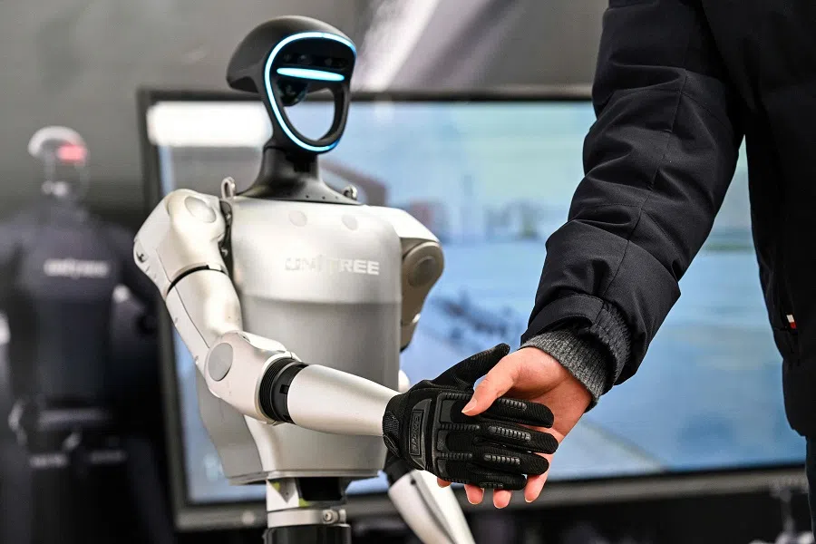 A man shakes hands with a humanoid robot from Unitree Robotics during the Global Developer Conference, organised by the Shanghai AI Industry Association, in Shanghai, China on 21 February 2025. (Hector Retamal/AFP)