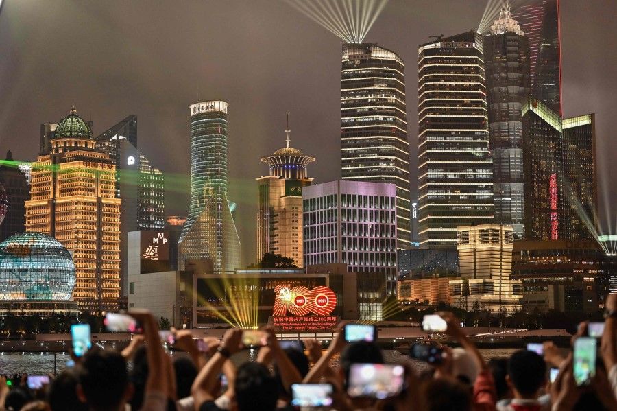 Spectators look at a light show on the Bund promenade in Shanghai on 1 July 2021, as the country marks the 100th anniversary of the founding of China's Communist Party. (Hector Retamal/AFP)