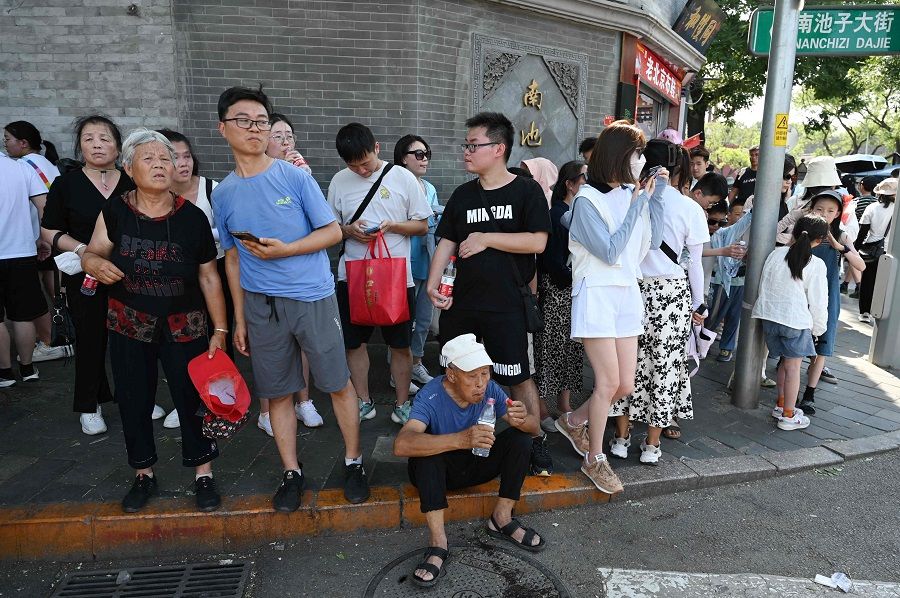 People wait in the shade on a street corner near the Forbidden City during a heatwave in Beijing, China, on 24 June 2023. (Greg Baker/AFP)