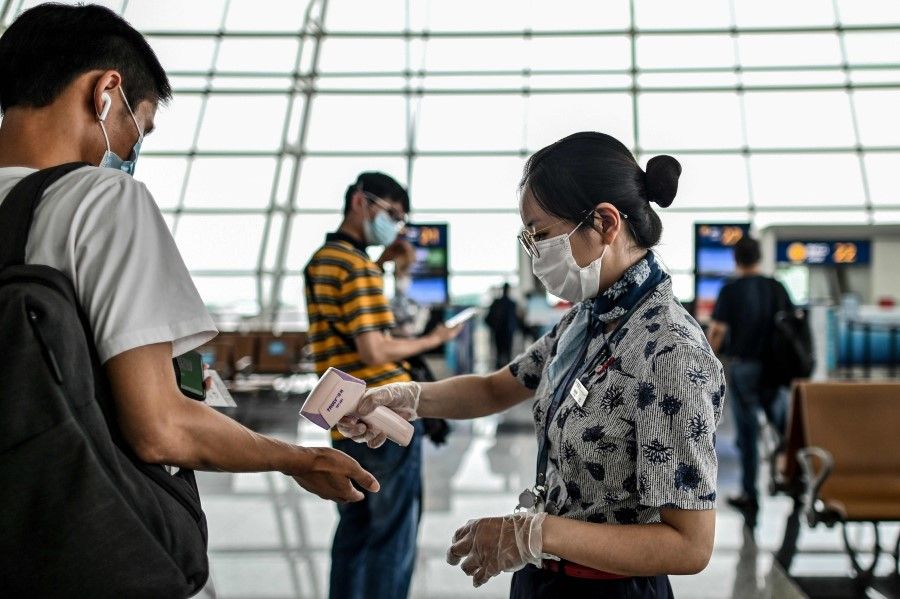 An airline worker (R) checks the body temperature of passengers in the boarding area at the Tianhe Airport in Wuhan, 29 May 2020. (Hector Retamal/AFP)
