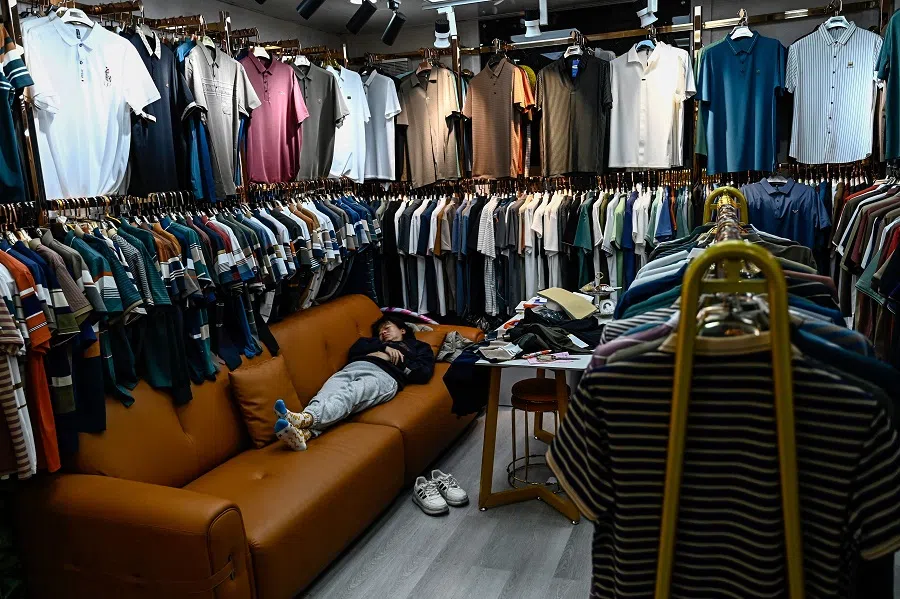This photo taken on 19 February 2025 shows an employee resting in a clothing shop at a wholesale export trade centre in Guangzhou, China’s southern Guangdong province. (Pedro Pardo/AFP)