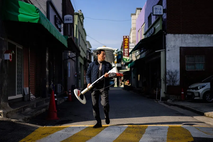 A man carries a portable heater as he walks down a street in Dongducheon, Gyeonggi province, about 38 kilometres north of Seoul, on 22 November 2023. (Anthony Wallace/AFP)