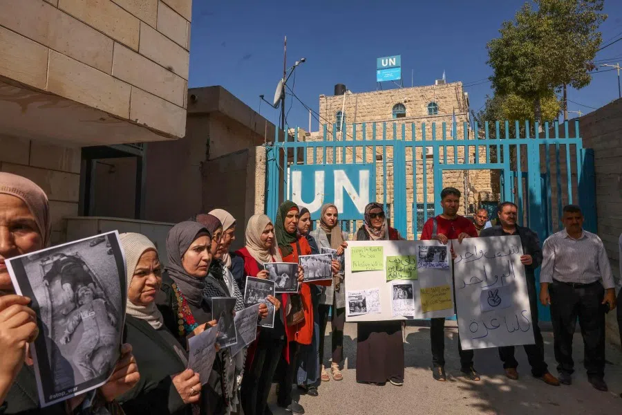 Palestinians lift placards during a rally in front of the United Nations Relief and Works Agency for Palestine Refugees (UNRWA) offices in Hebron in the occupied West Bank on 31 October 2023, in support of Gaza amid ongoing battles between Israel and the Palestinian group Hamas. (Hazem Bader/AFP)