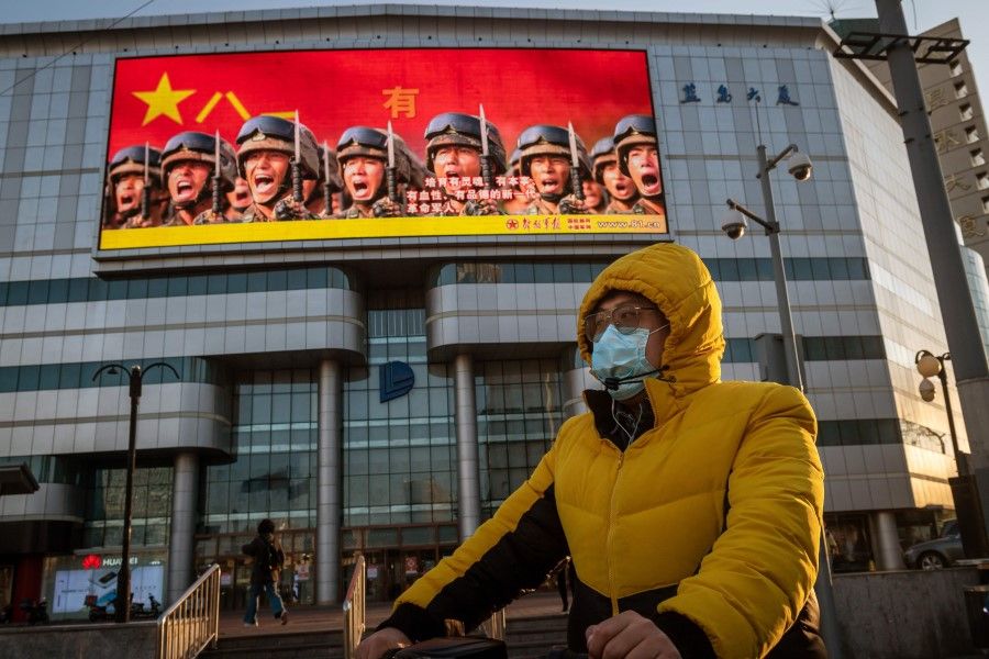 A man in front of a screen displaying a propaganda image (top), on a street in Beijing, April 20, 2020. (Nicolas Asfouri/AFP)