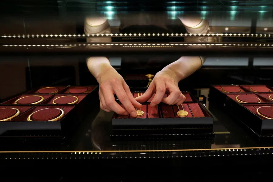 A staff member arranges gold necklaces in a display case at a Laopu Gold jewellery store in Beijing, China, 12 March 2025. (Florence Lo/Reuters)