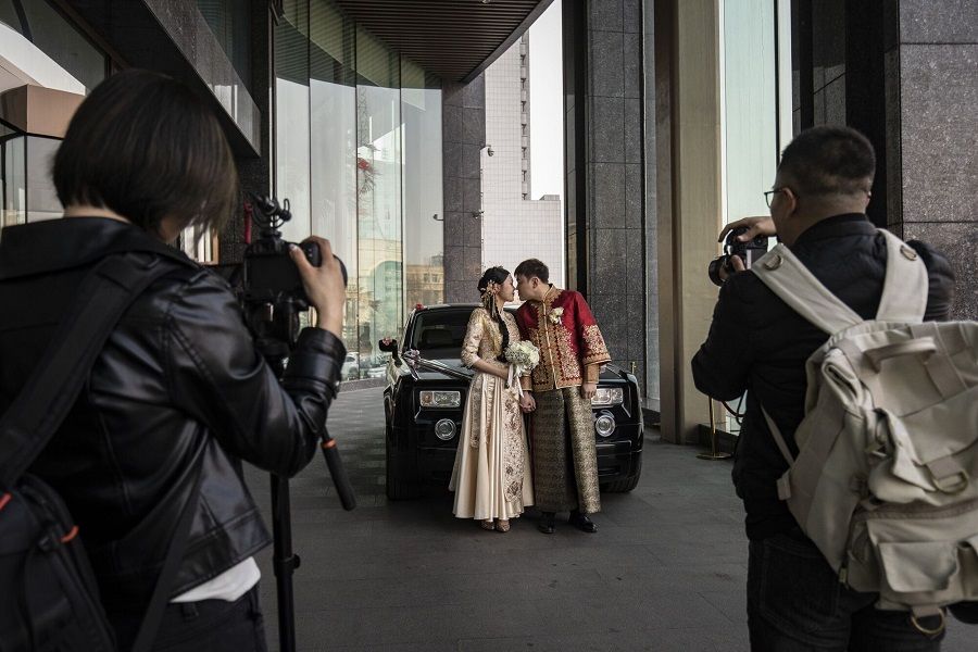 A newly wed couple have their pictures taken with family and friends as a rented Rolls Royce picks them up in front of a hotel in Hegang, China, on 2 April 2023. (Qilai Shen/Bloomberg)