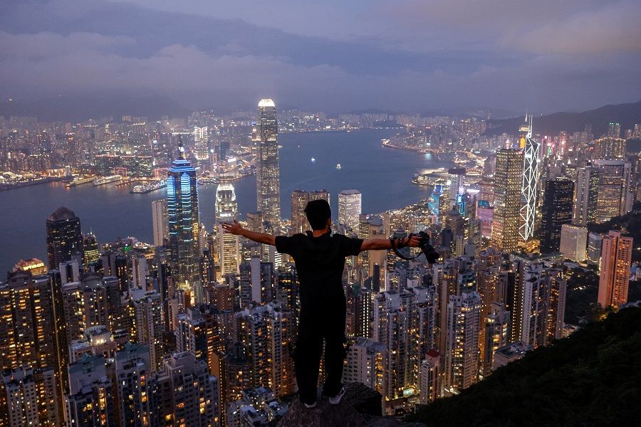 A person poses for a photo against the backdrop of the financial Central district and Victoria Harbour in Hong Kong, China, 9 May 2023. (Reuters/Tyrone Siu)