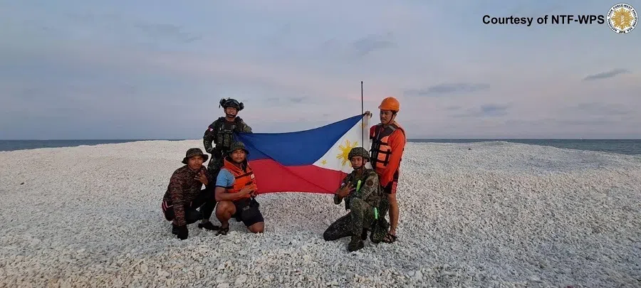 This handout photo taken on 27 April 2025, received on 28 April and released by the National Task Force on West Philippine Sea (NTF-WPS) through Philippine Coast Guard shows Philippine coast guard and military personnel holding a Philippine flag during an inter-agency maritime operation in Sandy Cay. (Handout/National Task Force on West Philippine Sea (NTF-WPS)/AFP)