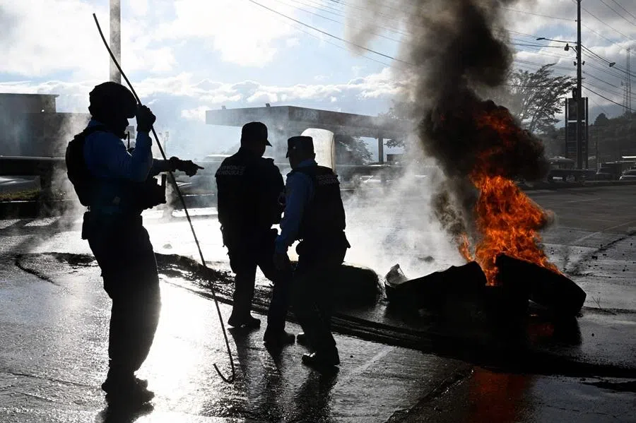 Honduran National Police members remove burning tyres set by supporters of the ruling Libertad y Refundacion (LIBRE) party to block the road connecting Tegucigalpa with northern Honduras, in Tegucigalpa on 24 December 2025. (Orlando Sierra/AFP)