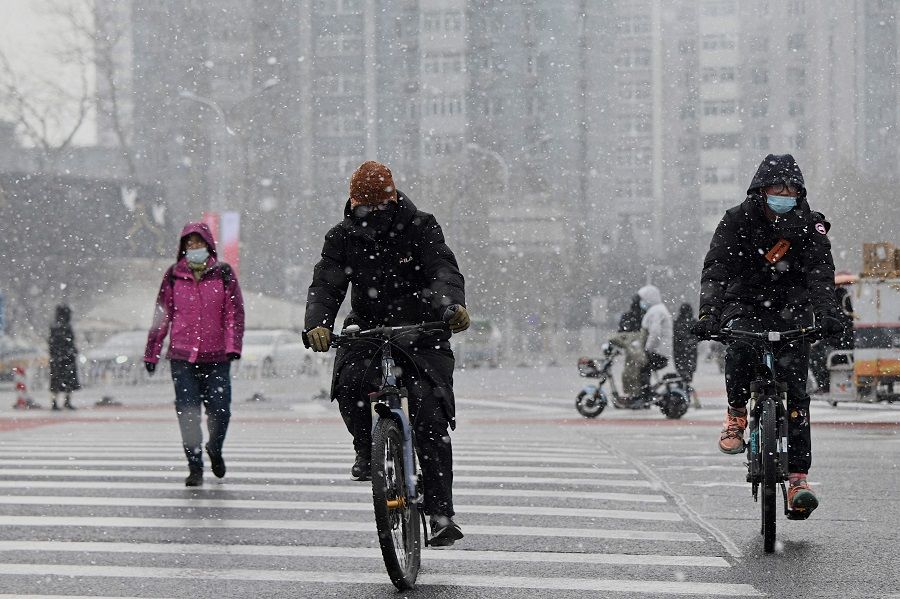 People ride their bicycles in the snow as they cross a street on a snowy day in Beijing, China, on 20 January 2022. (Noel Celis/AFP)