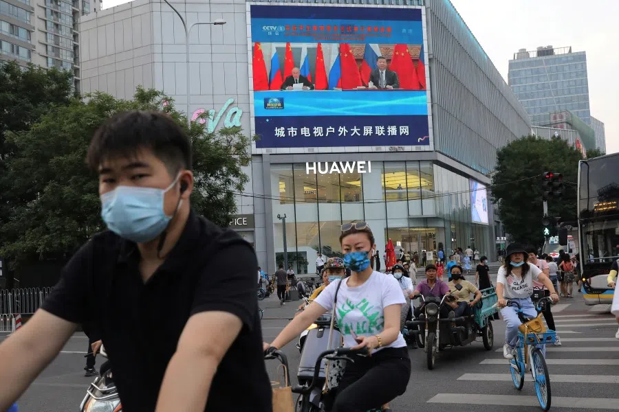 People cycle to cross a street near a giant screen broadcasting news footage of Chinese President Xi Jinping attending a video conference call with Russian President Vladimir Putin, in Beijing, China, 28 June 2021. (Tingshu Wang/Reuters)