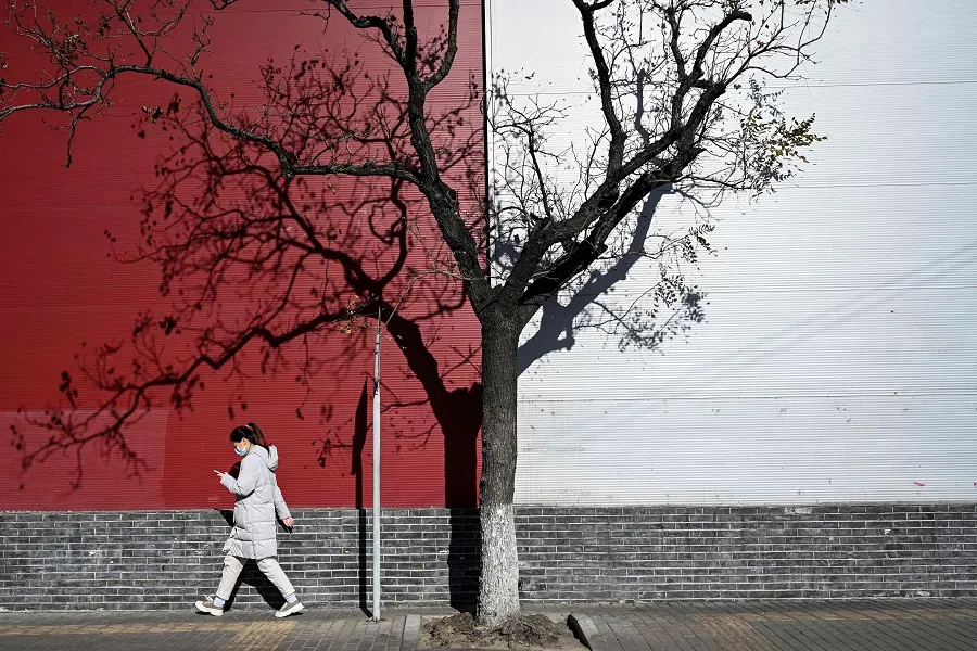 A woman walks past a tree on a street in Beijing on 23 November 2021. (Jade Gao/AFP)