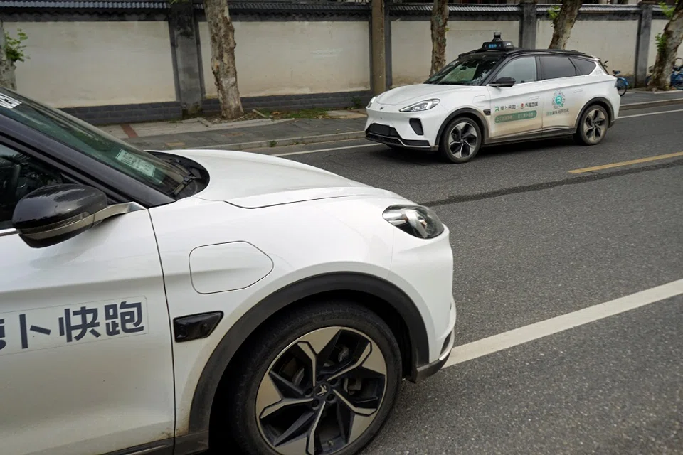 A driverless car by Apollo Go, Baidu’s robotaxi service, drives past another Apollo Go robotaxi parked on the side of a road in Wuhan, Hubei province, China, 19 July 2024. (Sarah Wu/Reuters)