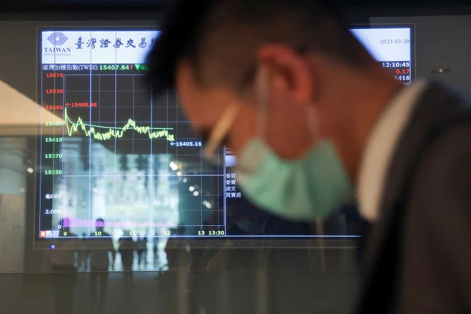 A man wearing a face mask passes in front of screens showing trading data while using an escalator outside Taiwan Stock Exchange in Taipei, Taiwan, on 20 March 2023.  (Annabelle Chih/Reuters)
