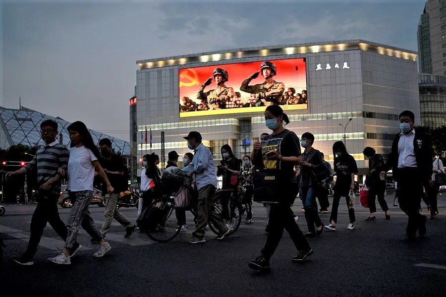 This photo taken on 18 May 2021 shows people walking along a street as military propaganda is displayed on a giant screen in Beijing, China. (Noel Celis/AFP)