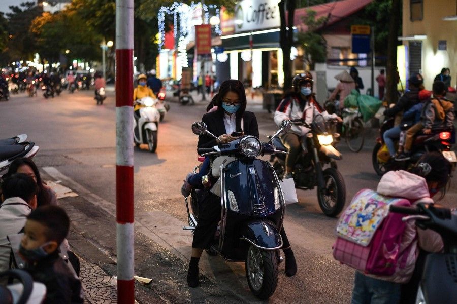 A woman wearing a facemask checks her smartphone while waiting on her scooter along a street in Hanoi on December 1, 2020, a day after Vietnam reported its first local transmission case of Covid-19 in nearly three months. (Photo by Manan VATSYAYANA / AFP)