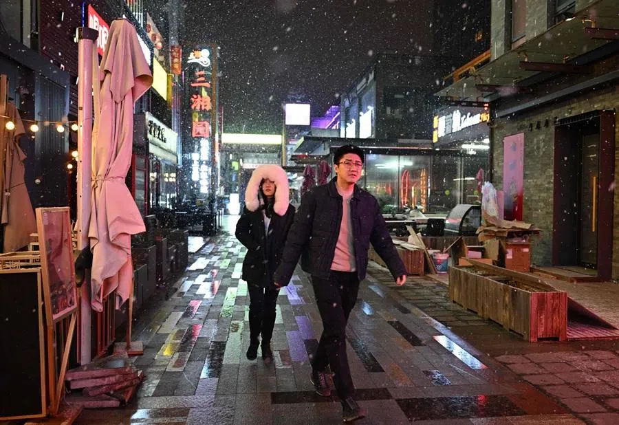 People walk past restaurants during snow fall in Beijing on 17 January 2026. (Adek Berry/AFP)