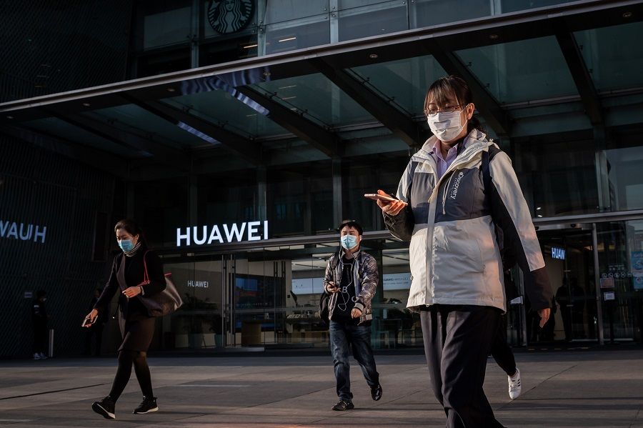 People wearing a wearing face masks as a preventive measure against the Covid-19 coronavirus walk outside a shopping mall past a Huawei shop in Beijing on 1 April 2020. Huawei rotating and acting Chairman Eric Xu predicted that 2020 would be Huawei's "most difficult year" yet. (Nicolas Asfouri/AFP)