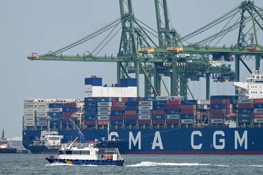 A boat sails past a container vessel docked at Pasir Panjang port terminal in Singapore on 9 July 2025. (Roslan Rahman/AFP)