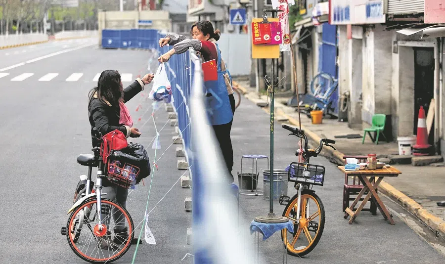 This photo taken on 16 March 2020 shows a woman delivering food to a resident over a barrier set up to prevent people from entering or leaving a residential community in Wuhan, Hubei province, China. (STR/AFP)