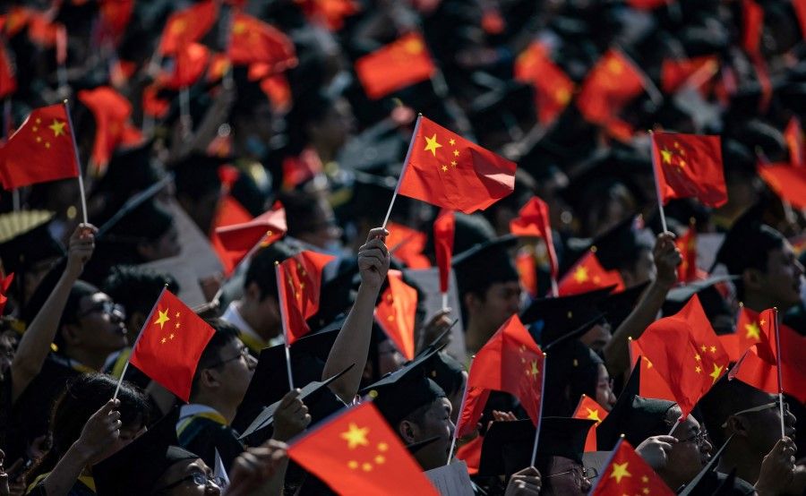 Graduates of Wuhan University wave national flags as they attend the graduation ceremony in Wuhan, in China's central Hubei province on 23 June 2021. (STR/AFP)
