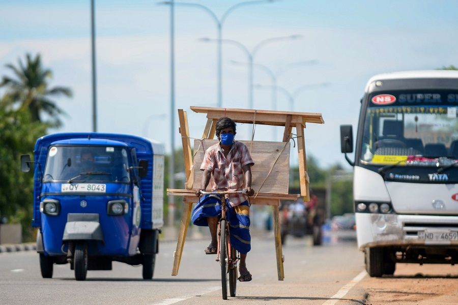 A man wearing a face mask transports wooden furniture on his bicycle along a street on the outskirts of Colombo, Sri Lanka, on 13 November 2020. (Lakruwan Wanniarachchi/AFP)