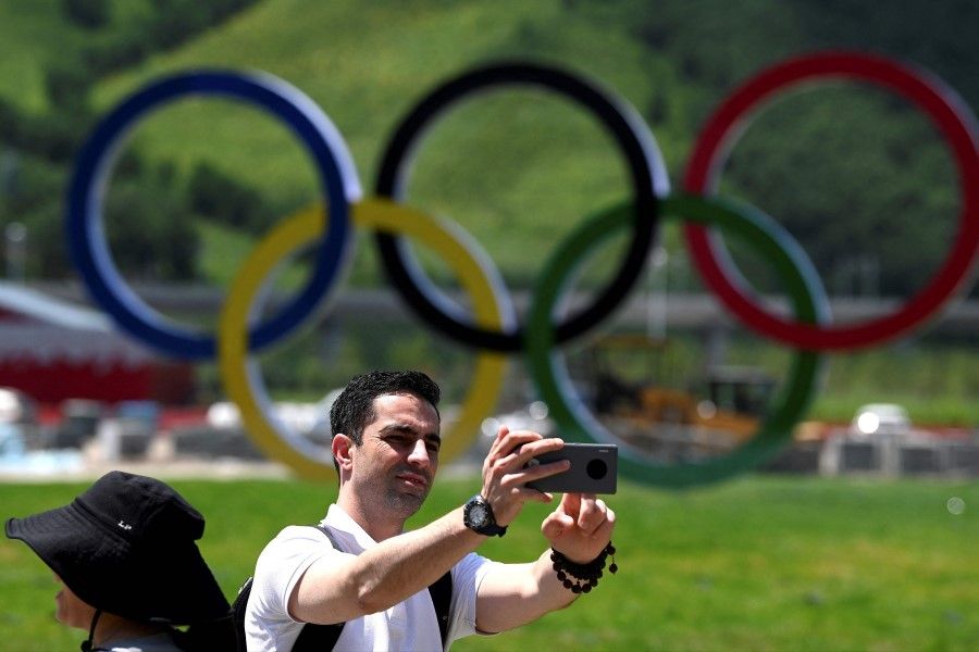 This file photo taken on 14 July 2021 shows a man taking a selfie near the Olympic rings at the athletes' village for the Beijing 2022 Winter Olympic Games in Zhangjiakou, in northern China's Hebei province. (Noel Celis/AFP)