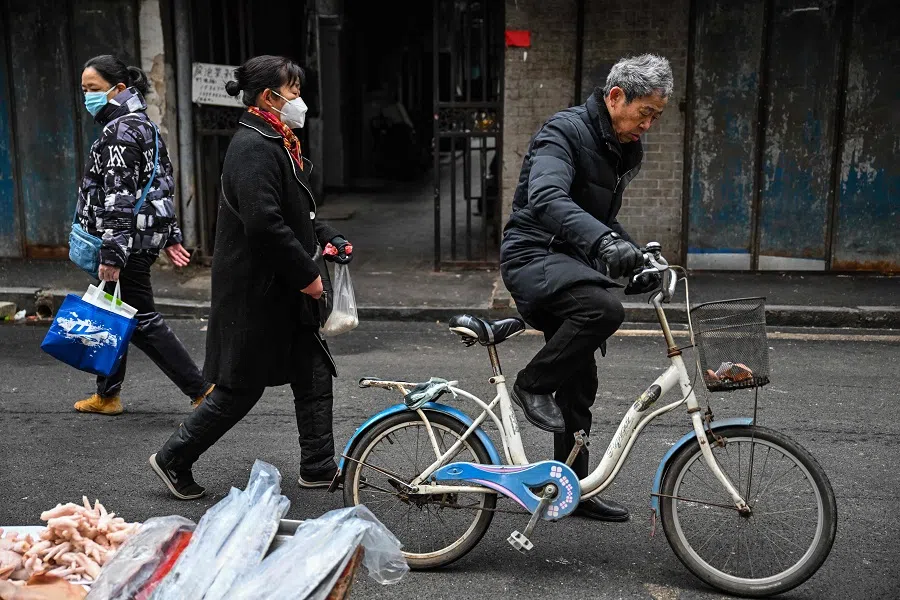 People walk down a street next to a local market in Wuhan, Hubei province, China, on 23 January 2023. (Hector Retamal/AFP)