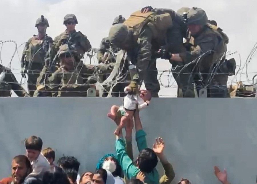 A baby is handed over to the American army over the perimeter wall of the airport for it to be evacuated, in Kabul, Afghanistan, 19 August 2021, in this still image taken from video obtained from social media. (Omar Haidari via Reuters)
