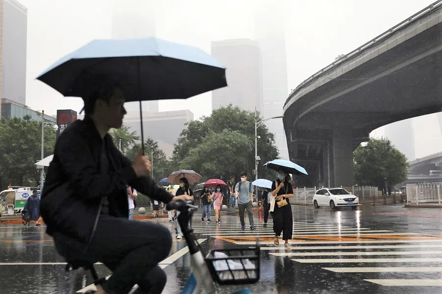 People are seen amid heavy rainfall during morning rush hour in Beijing's Central Business District, China, 12 July 2021. (Tingshu Wang/Reuters)