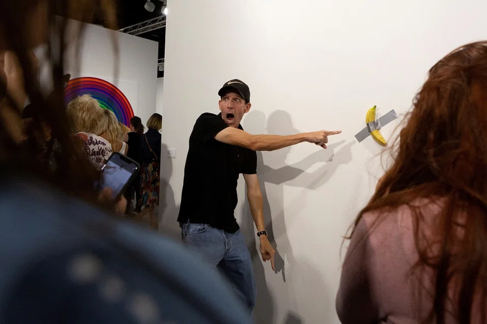 A man poses for a photo next to a banana attached with duct-tape that replaces the artwork “Comedian” by the artist Maurizio Cattelan, which was eaten by David Datuna, in Miami Beach, Florida, US, on 7 December 2019. (Eva Marie Uzcategui/Reuters)