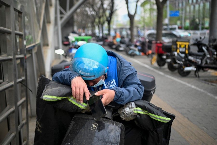 A food delivery worker rests on his electric bicycle by a roadside in Beijing on 1 April 2023. (Wang Zhao/AFP)