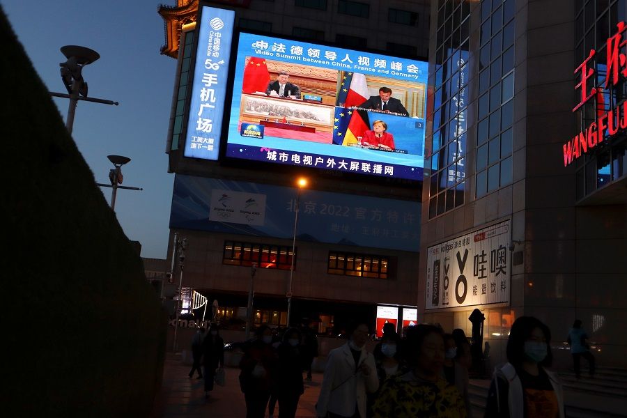 A giant screen shows news footage of Chinese President Xi Jinping attending a video summit on climate change with German Chancellor Angela Merkel and French President Emmanuel Macron, at a shopping street in Beijing, China, 16 April 2021. (Florence Lo/Reuters)