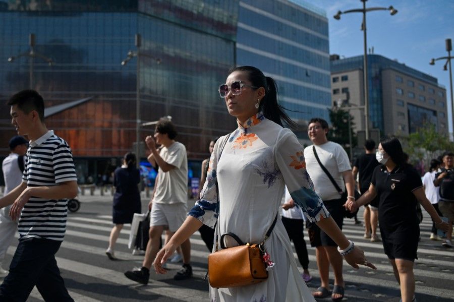 Pedestrians cross a street at a business district in Beijing on 14 August 2023. (Wang Zhao/AFP)