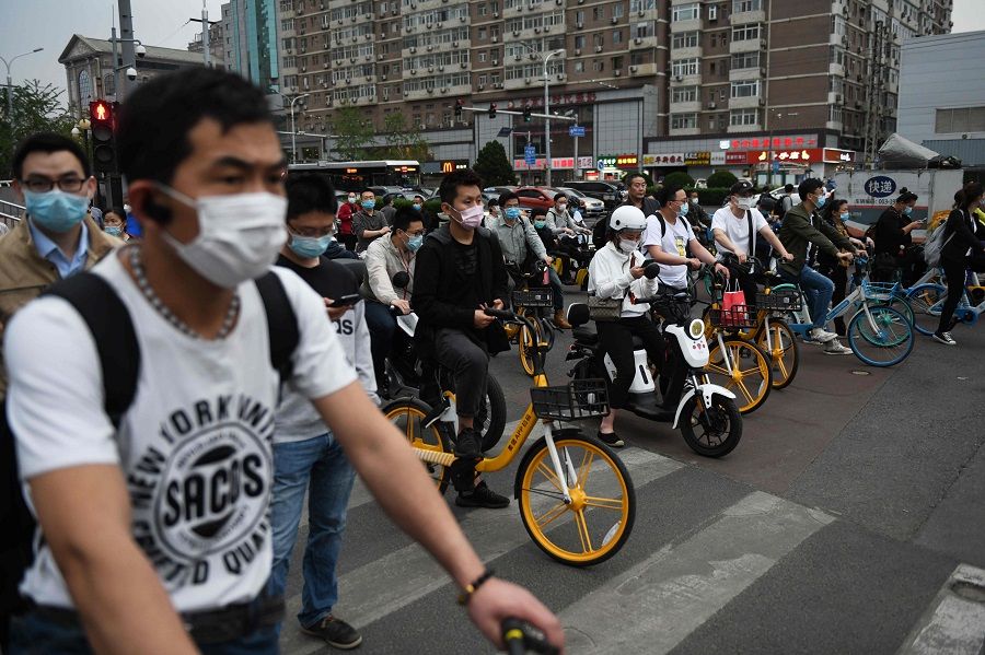 People wear face masks as a precaution against the Covid-19 coronavirus as they wait to cross a road during rush hour in Beijing on 15 May 2020. (Greg Baker/AFP)