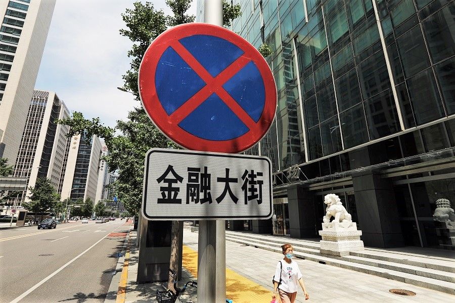 A woman walks past a sign of the Financial Street in Beijing, China, 9 July 2021. (Tingshu Wang/Reuters)
