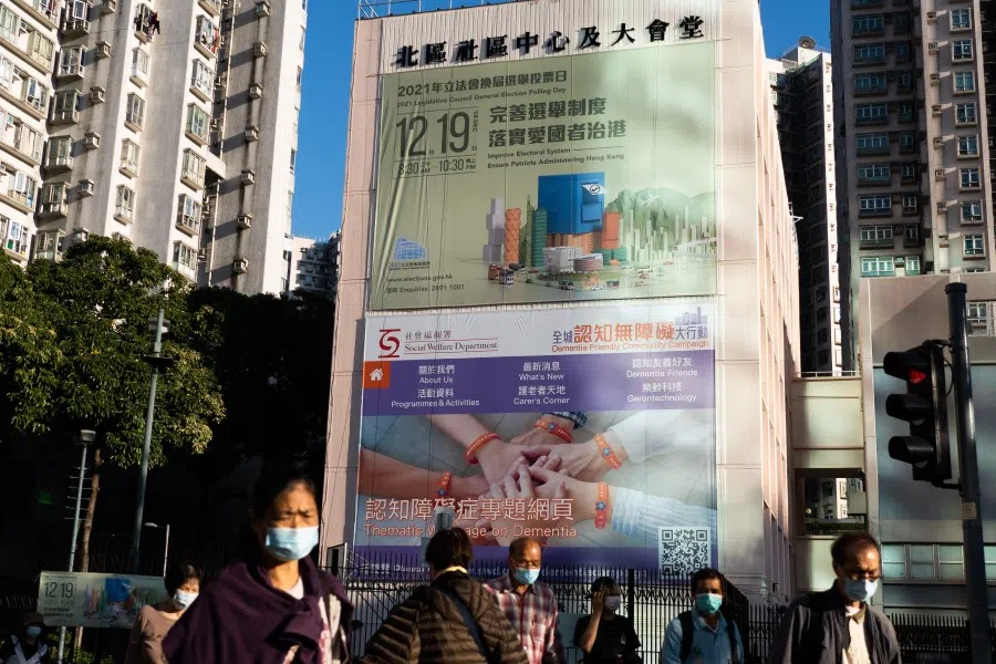 People walk past a government banner for the upcoming 19 December Legislative Council election in Hong Kong on 10 December 2021. (Bertha Wang/AFP)