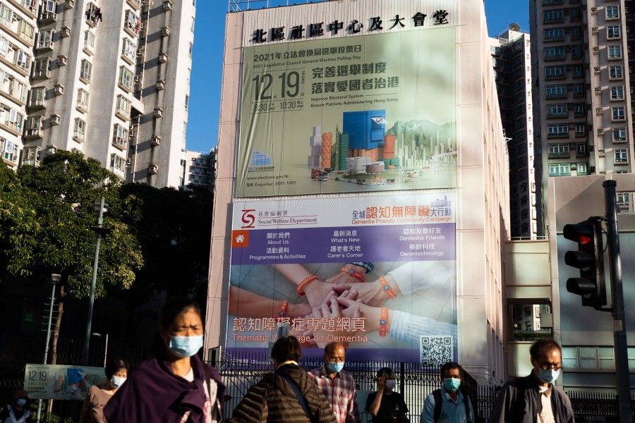 People walk past a government banner for the upcoming 19 December Legislative Council election in Hong Kong on 10 December 2021. (Bertha Wang/AFP)