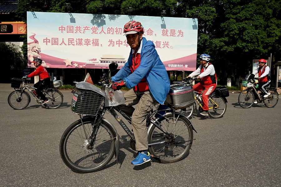 This photo taken on 22 May 2021 shows people cycling in front of a poster that reads "The original intention and mission of the Chinese Communists is to seek happiness for the Chinese people and rejuvenation for the nation", along a street in Huaxi village, Jiangsu province, China. (Noel Celis/AFP)