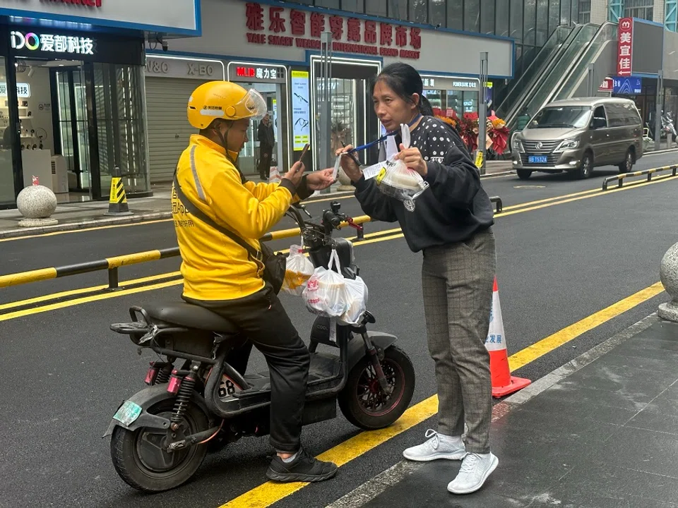 A delivery rider scanning the QR payment code hanging around the neck of a substitute delivery auntie.