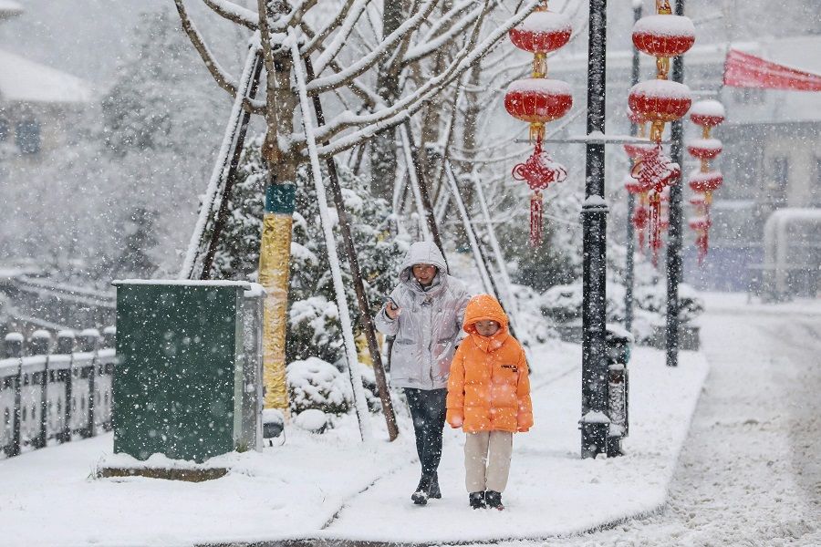 Residents taking a walk as snow falls in Hangzhou, Zhejiang province, China, 7 February 2022. (AFP)