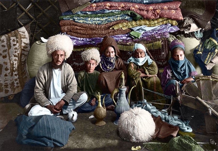A Tajik family sits cross-legged on a carpet, early 20th century. Pots of tea are laid out in front of the male host to welcome guests.