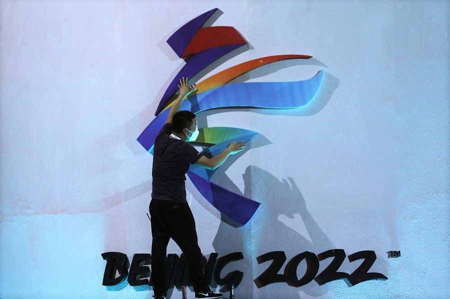 A man adjusts an emblem of the Beijing 2022 Winter Olympic Games before a ceremony unveiling the slogan, in Beijing, China, 17 September 2021. (Tingshu Wang/Reuters)
