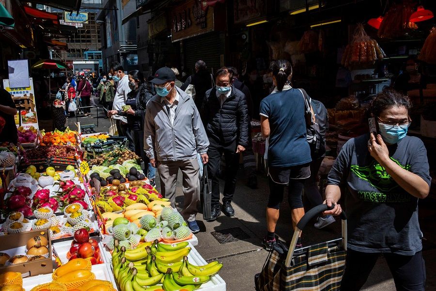 People wearing face masks walk through a market in Hong Kong on 3 March 2022. (Isaac Lawrence/AFP)