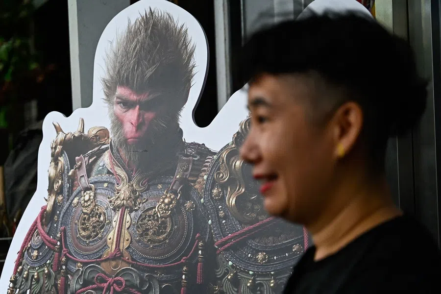 A woman stands next to a cardboard cutout of the Monkey King character, or Sun Wukong, of the Chinese action role-playing game Black Myth: Wukong during its launch day in Beijing on 20 August 2024.