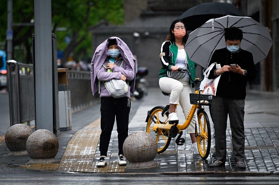 People wait to cross a street on a rainy day in Beijing, China, on 6 May 2022. (Wang Zhao/AFP)