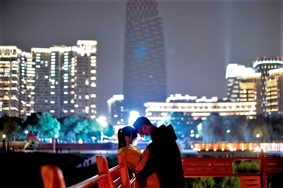 A couple wearing face masks cuddles along a park at the Yangtze river in Wuhan, Hubei, on 12 April 2020. (Noel Celis/AFP)