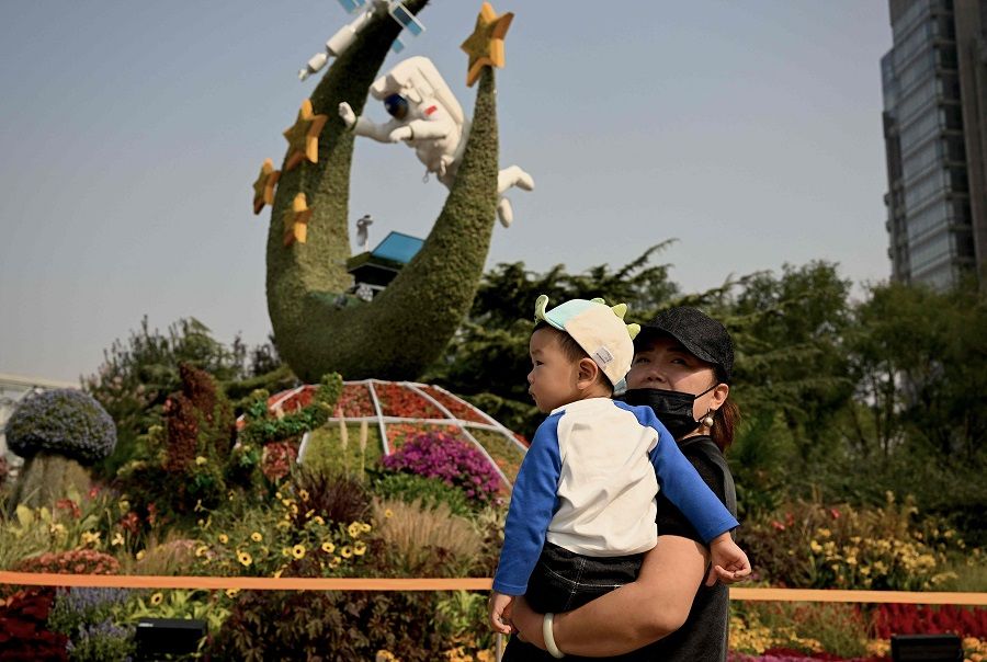 A woman carrying a boy walks past a flower display depicting China's space programme in Beijing, China, on 27 September 2022. (Noel Celis/AFP)